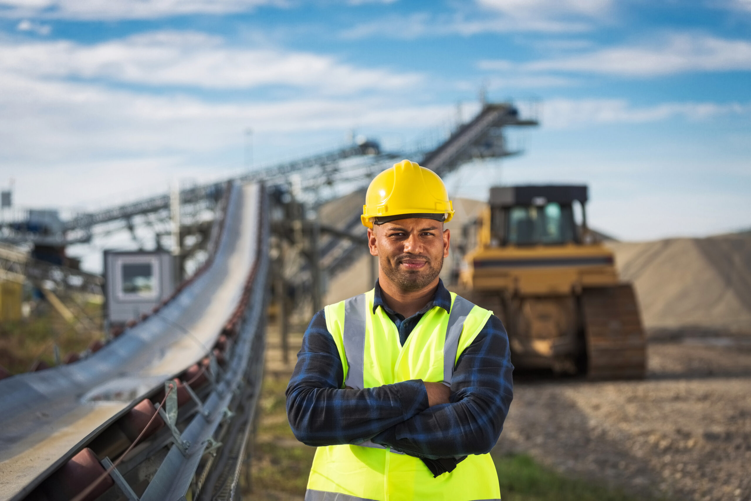 Photo of a man wearing a hard hat in front of a conveyor at a mining facility